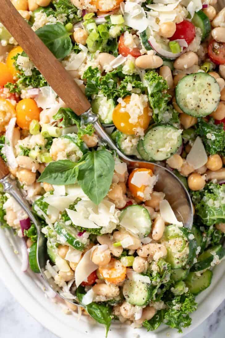 A white oval platter filled with white bean quinoa salad. Salad servers with wooden handles rest on the platter.