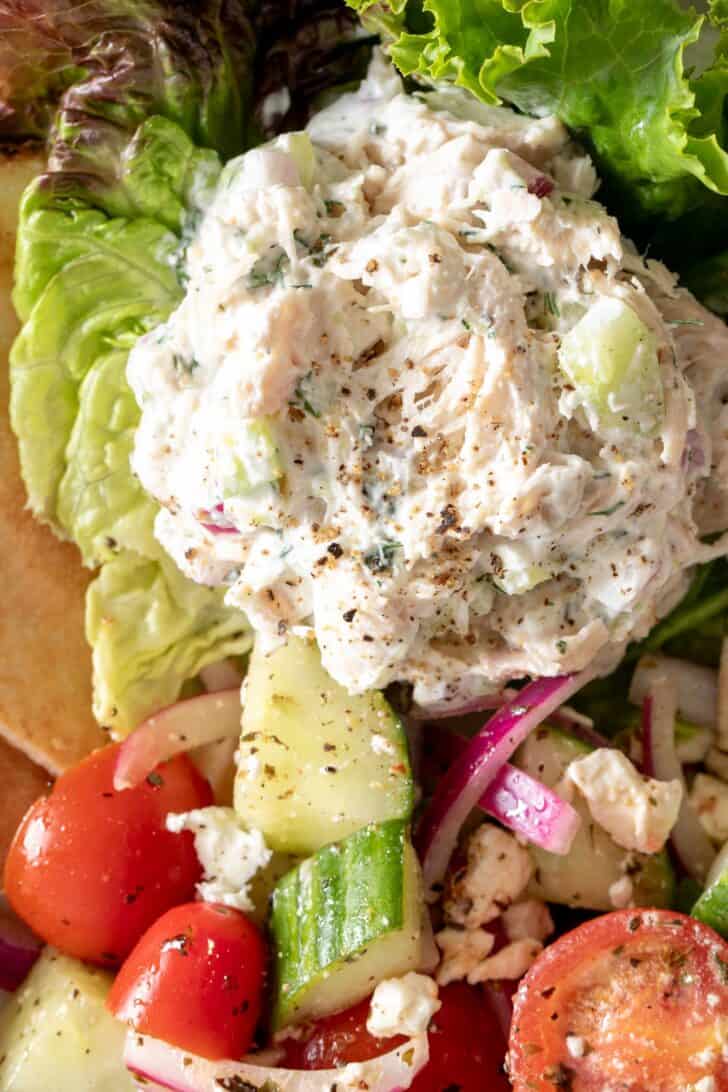 A scoop of Tzatziki Chicken Salad on a bed of lettuce next to a cucumber tomato salad.