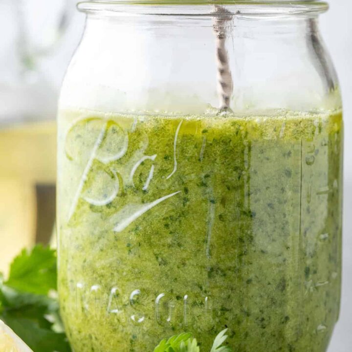 A clear glass mason jar filled with Cilantro Pesto. A silver spoon rests in the jar.