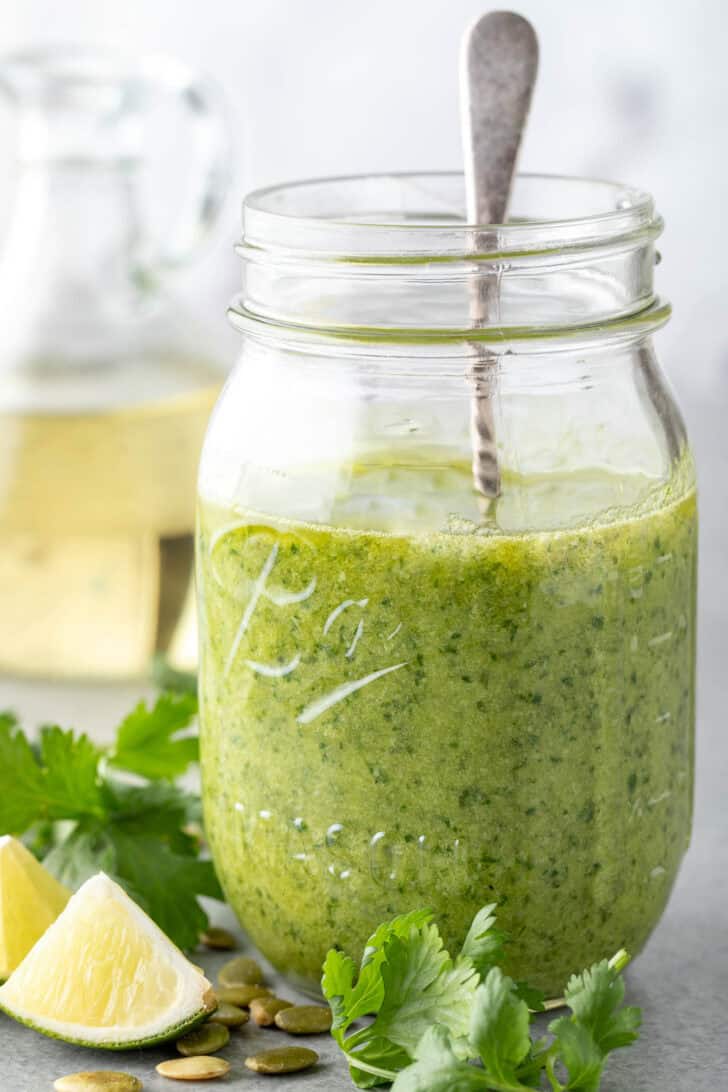 A clear mason jar filled with green sauce. A silver spoon rests in the jar.