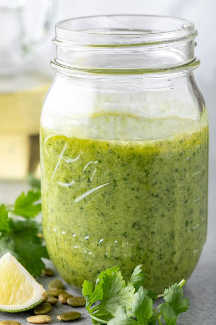 A clear glass mason jar filled with cilantro pumpkin seed pesto sauce.