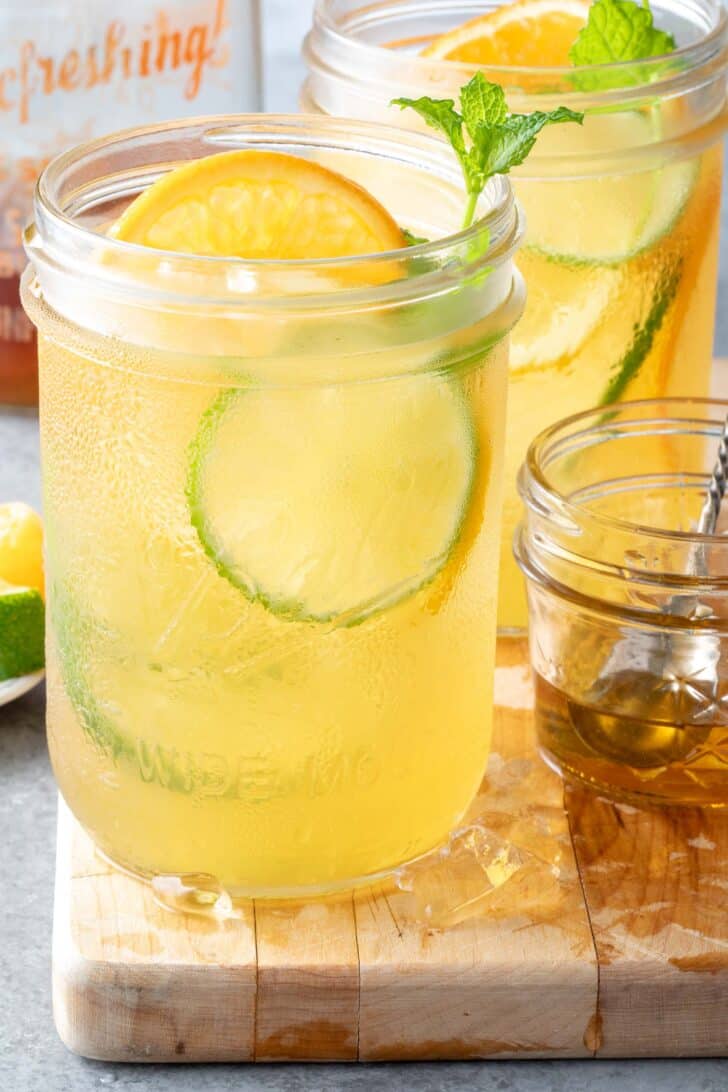 Two clear glass mason jars filled with liquid and citrus slices sit on a wood cutting board.