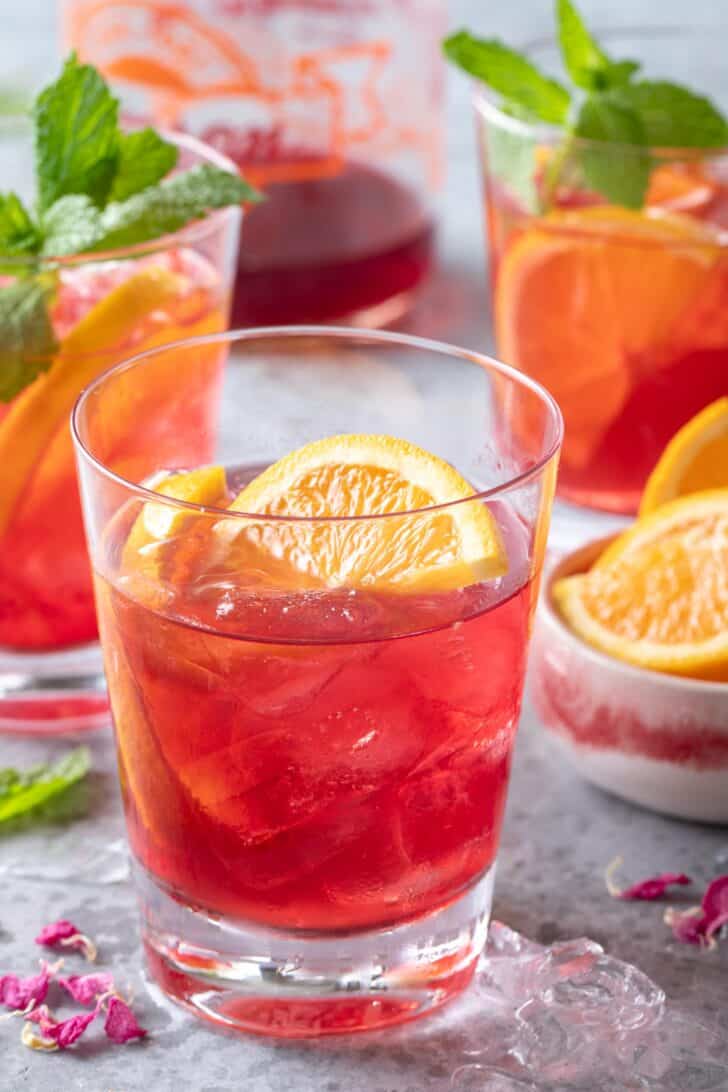 Three clear drinking glasses filled with a fruit juice drink with orange slices. 