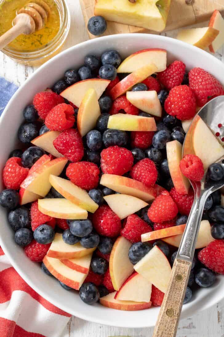 A white bowl filled with Red White and Blue Fruit Salad made with raspberries, blueberries and apples.