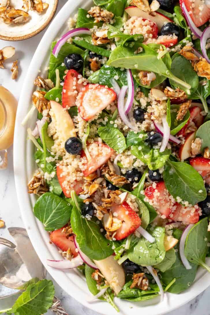 A white platter filled with mixed greens, quinoa and fruit.