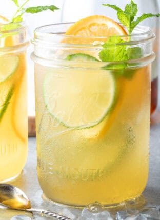 Two clear mason jars filled with Fruit Infused Iced Green Tea. A small spoon filled with honey sits next to the mason jars.