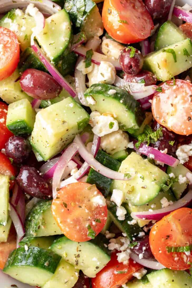 A white bowl filled with Greek Cucumber Salad tossed in vinaigrette.