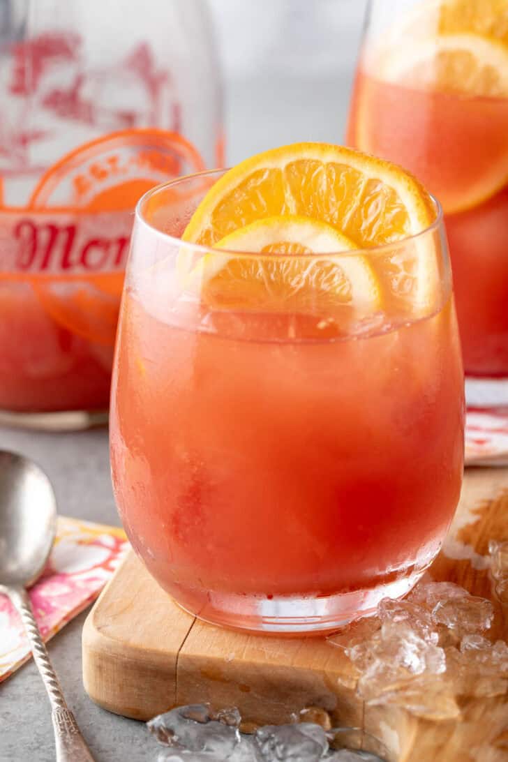 Two clear drinking glasses filled with pink juice. Ice is scattered ear the glasses.