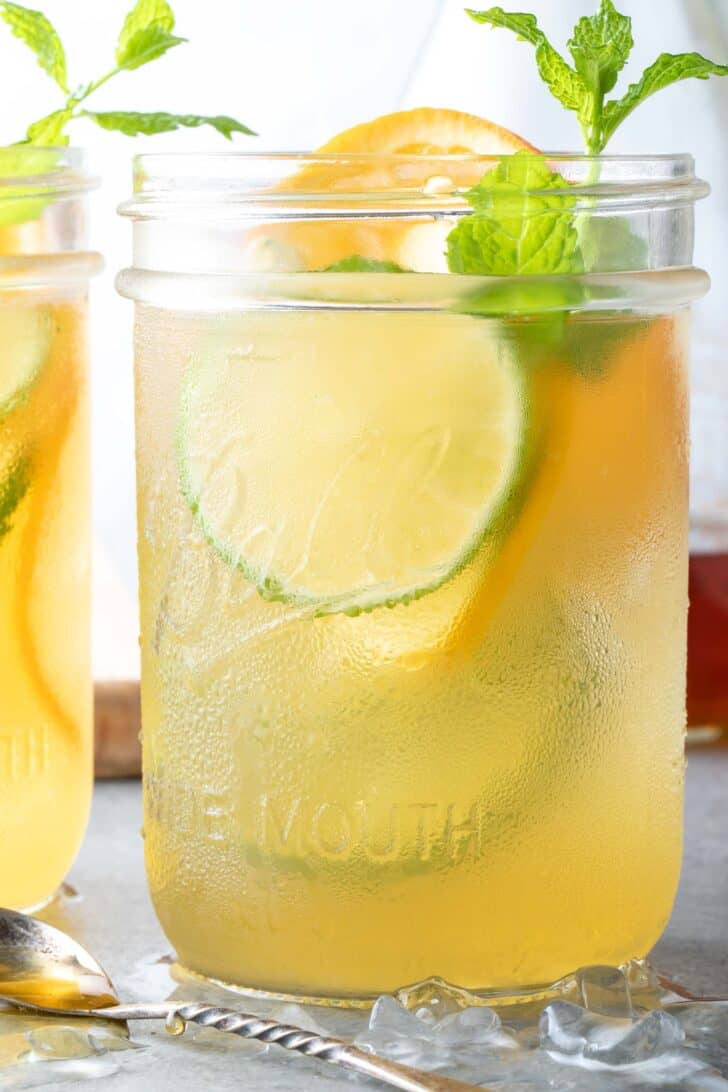 Two clear glass mason jars filled with iced green tea and citrus slices sit on a wood cutting board.