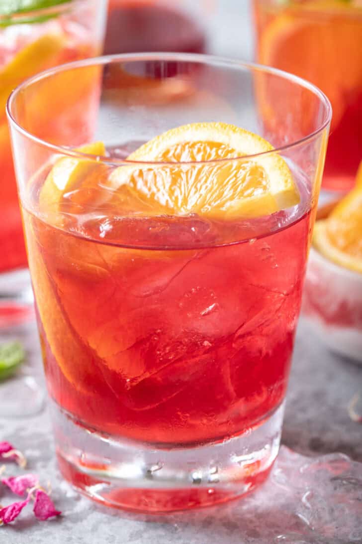 A clear drinking glass filled with Iced Cranberry Orange Green Tea.