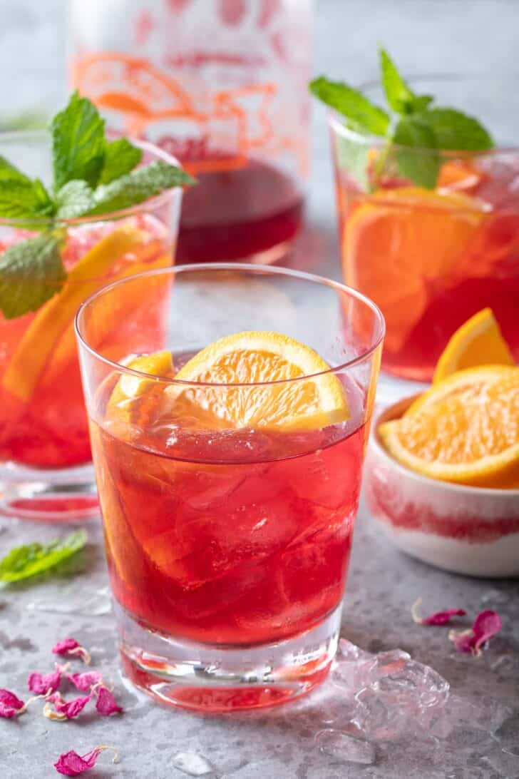 Three clear drinking glasses filled with a fruit juice drink with orange slices. 