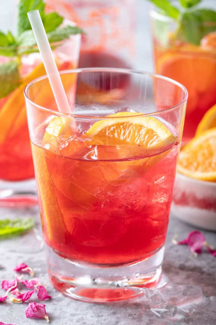 A clear drinking glass filled with Iced Cranberry Orange Green Tea.