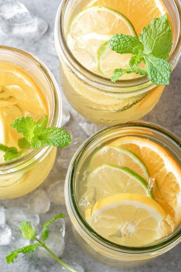 Three clear glass mason jars filled with liquid and slices of citrus and sprigs of fresh mint.