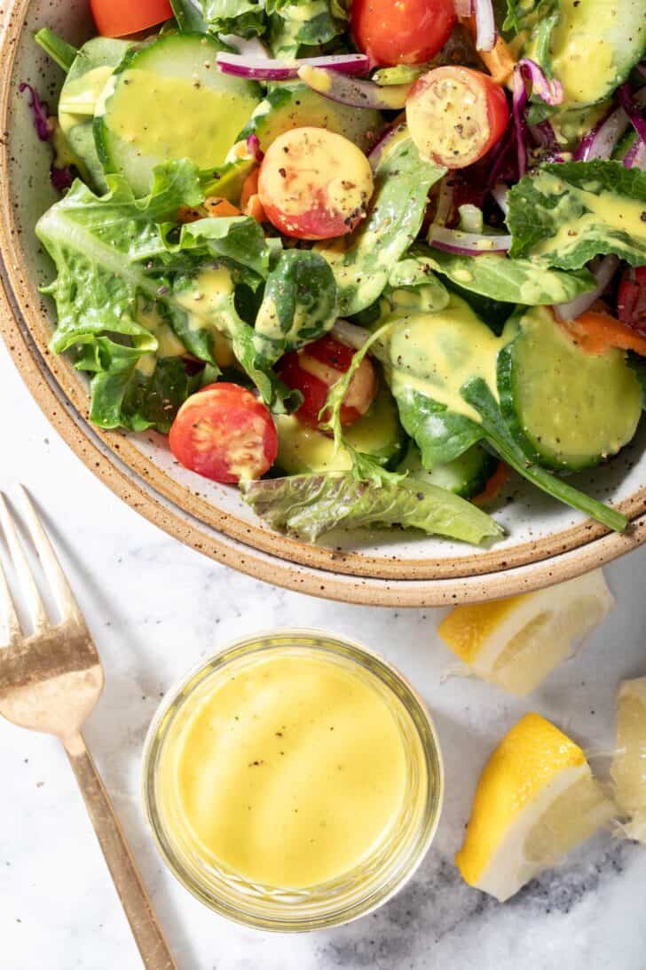 A tan colored bowl filled with mixed greens, cherry tomato slices and cucumber slices tossed in a vinaigrette.