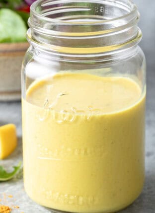 A clear glass mason jar filled with Turmeric Lemon Tahini Dressing.