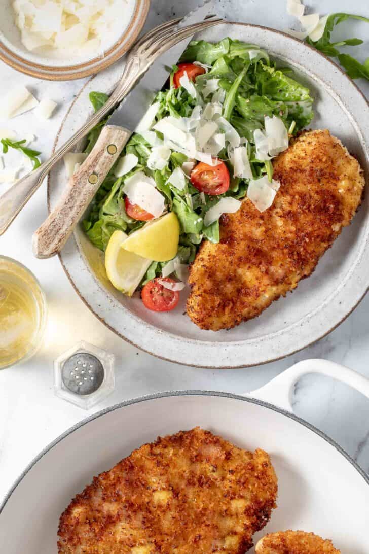 A white plate filled with cooked poultry and an arugula salad.