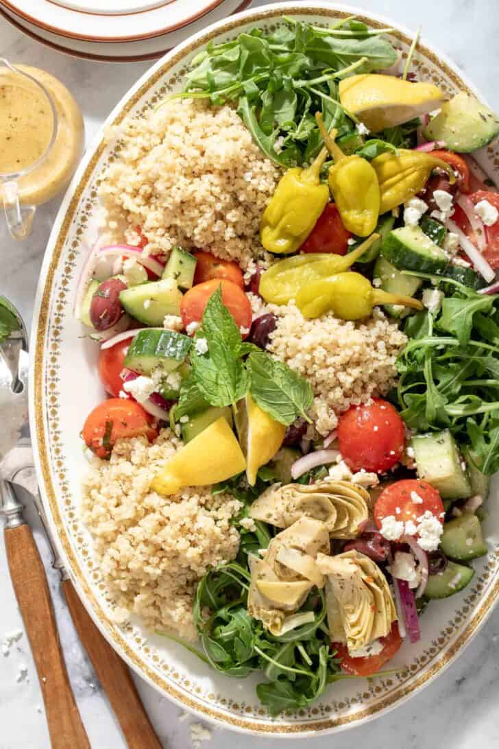 An oval white platter filled with mixed greens and chopped vegetables. 