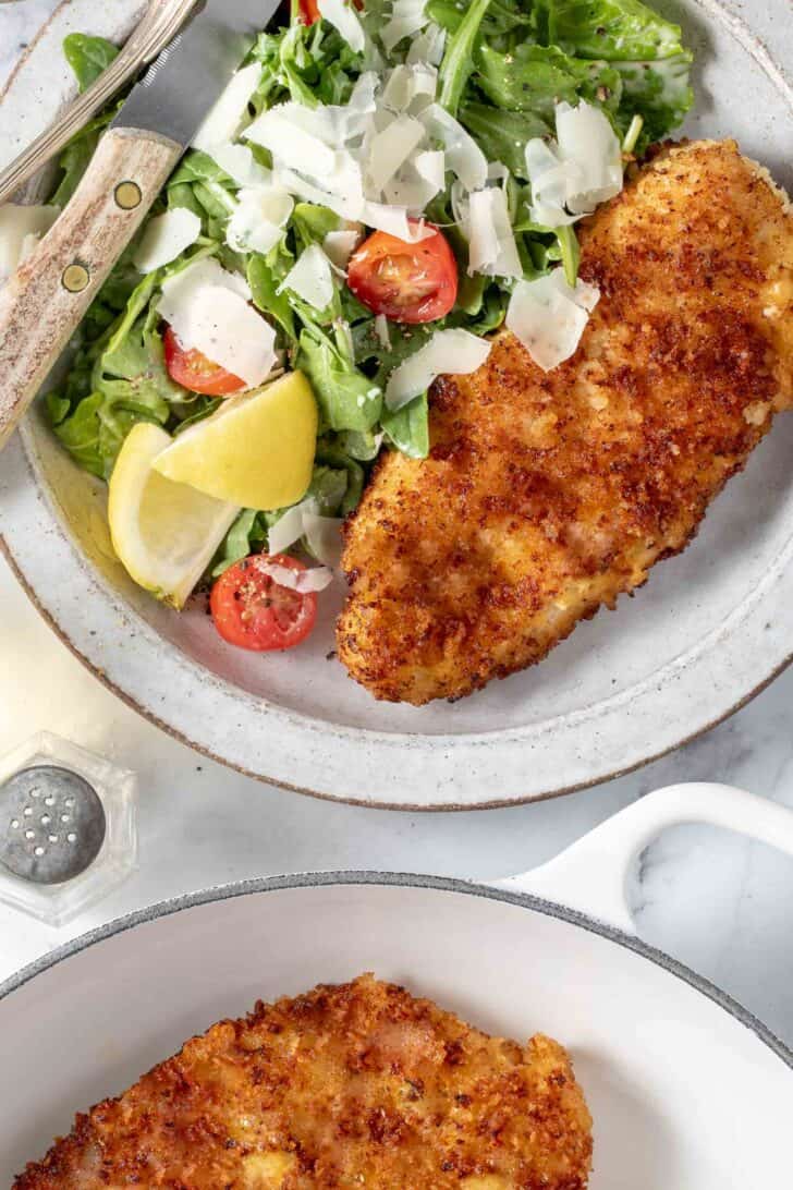 A white plate filled with arugula salad and Parmesan crusted chicken cutlets.