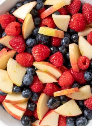A white bowl filled with Red White and Blue Fruit Salad made with raspberries, blueberries and apple.