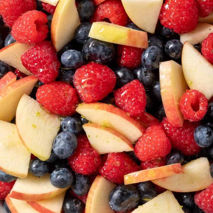 A white bowl filled with Red White and Blue Fruit Salad made with raspberries, blueberries and apple.