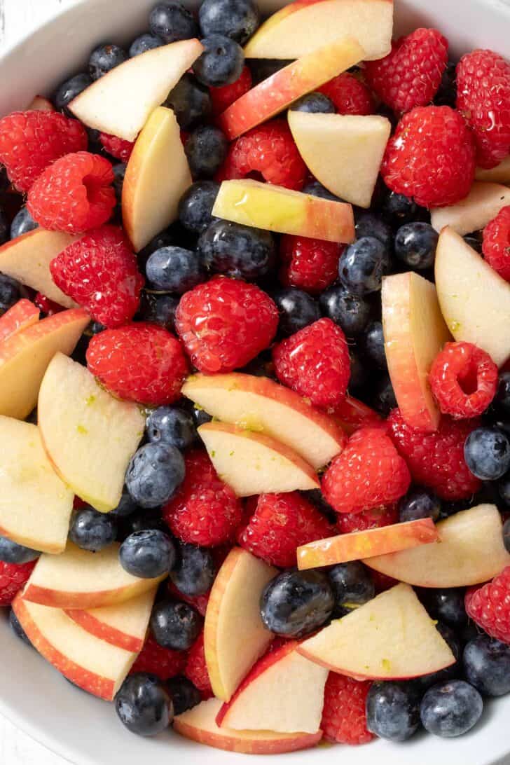 A white bowl filled with Red White and Blue Fruit Salad made with raspberries, blueberries and apple.