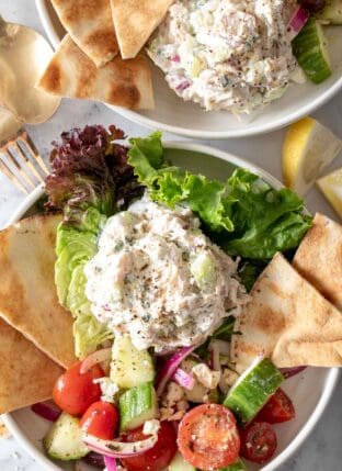 Two white plates filled with scoops of Tzatziki Chicken Salad on lettuce with pita bread.