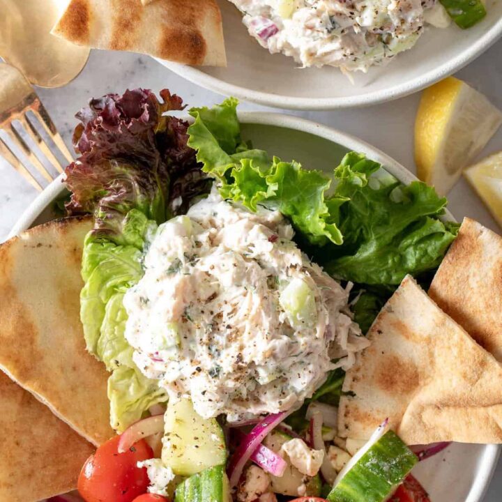 Two white plates filled with scoops of Tzatziki Chicken Salad on lettuce with pita bread.