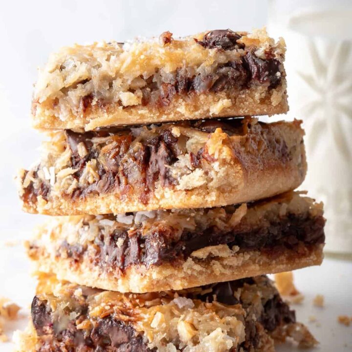 A stack of four Magic Cookie Bars next to a small glass of milk.