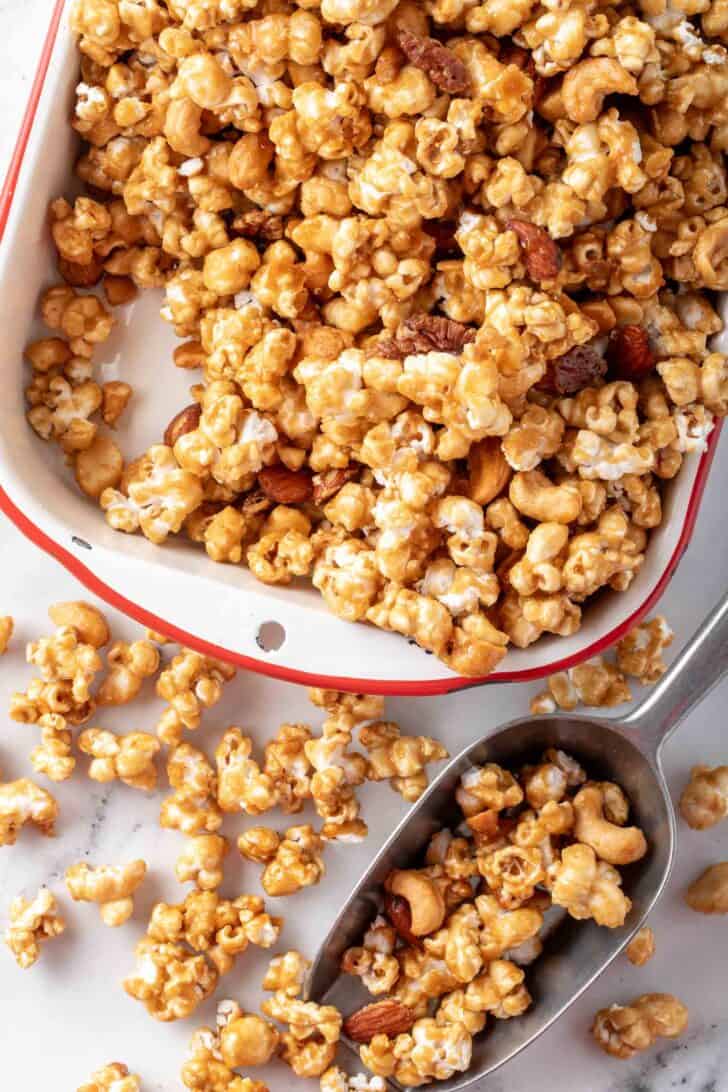 A white tray frilled with a candied nut mix. A metal scoop sits next to the tray.