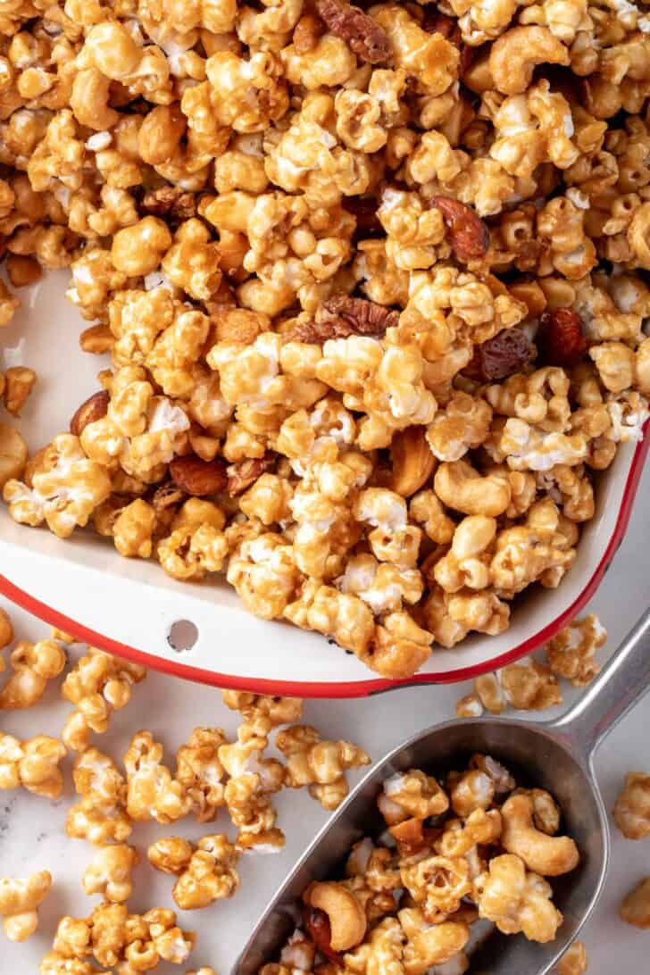 A white tray filled with Caramel Corn Popcorn. A metal scoop sits next to the tray.