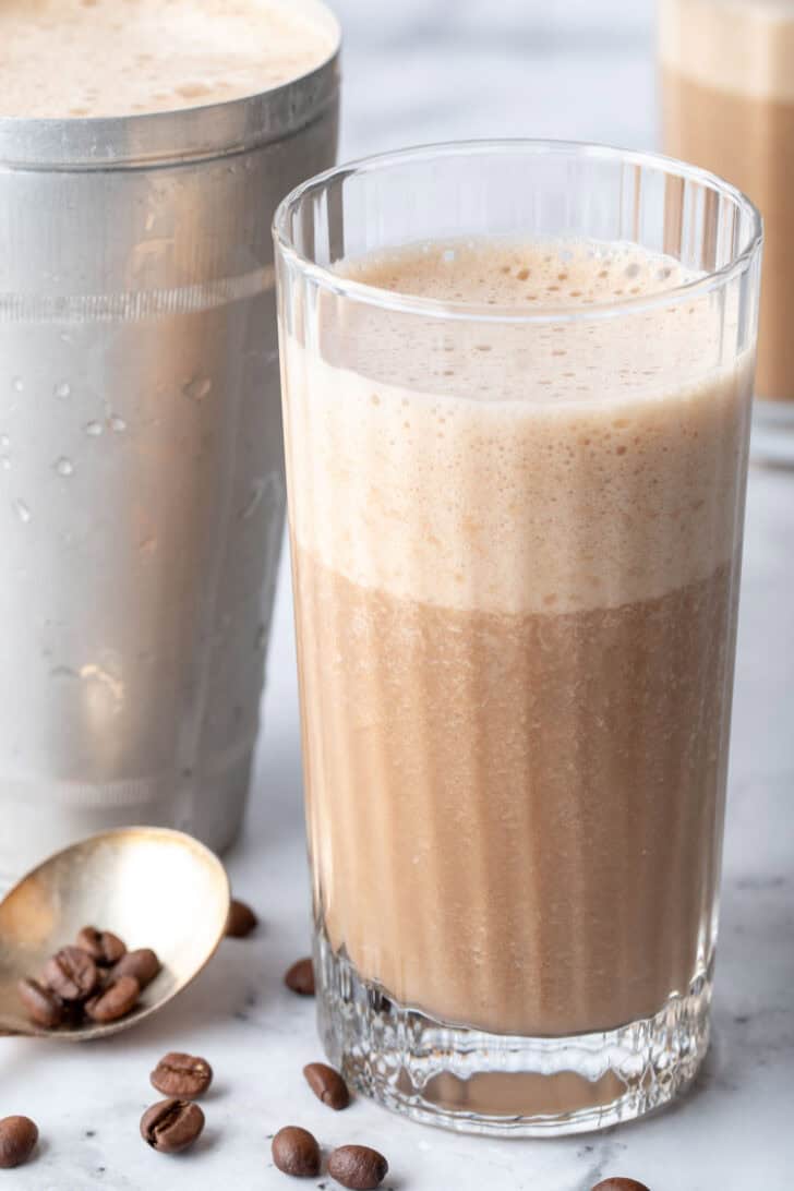 A clear drinking glass filled with a creamy frothy mocha drink.