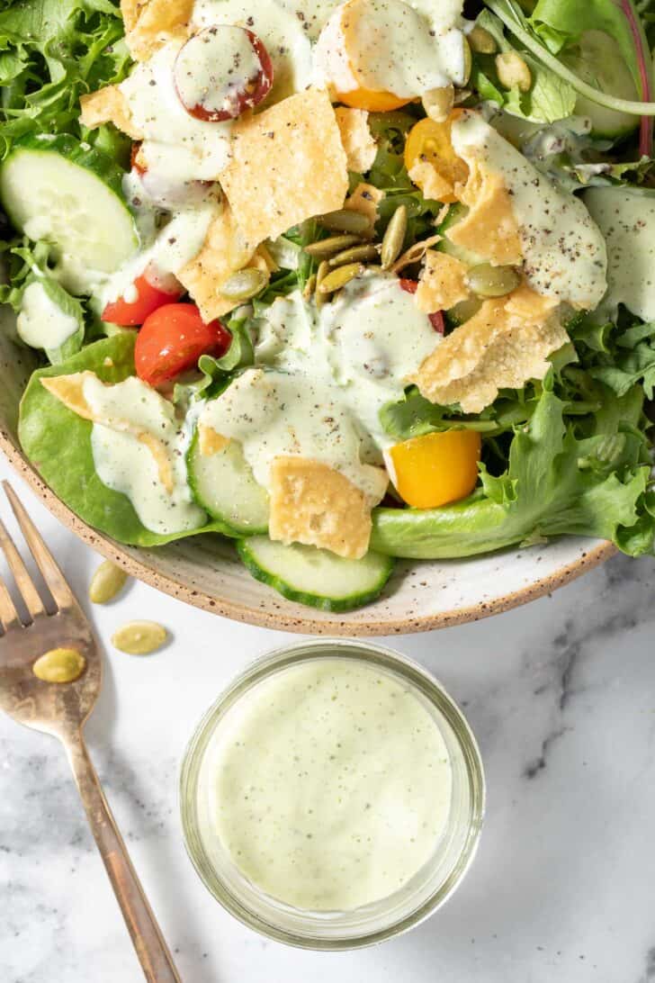 A tan colored bowl filled with mixed greens, cherry tomatoes, cucumber slices and tortilla chips.