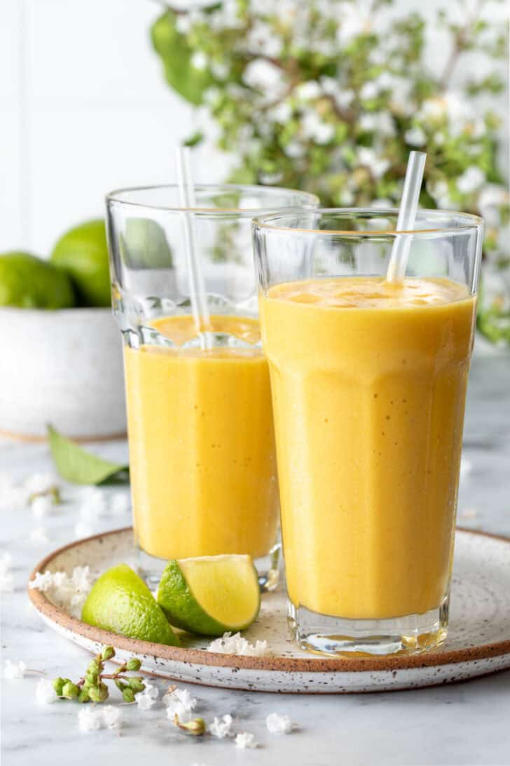 Two clear drinking glasses filled with mango smoothies.