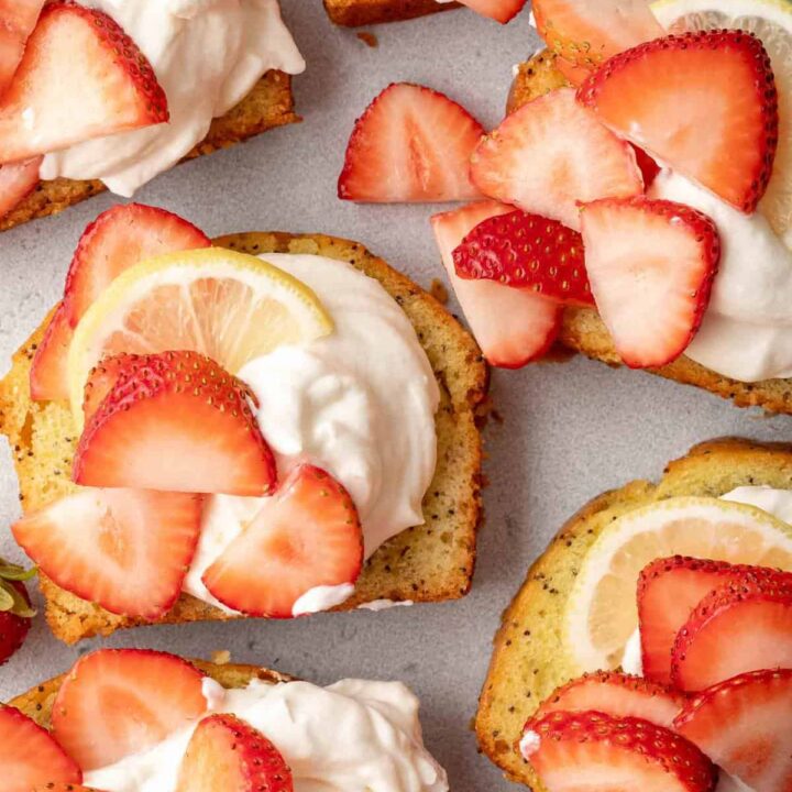 Slices of pound cake topped with Mascarpone Whipped Cream. Slices of strawberries are scattered over the cream.