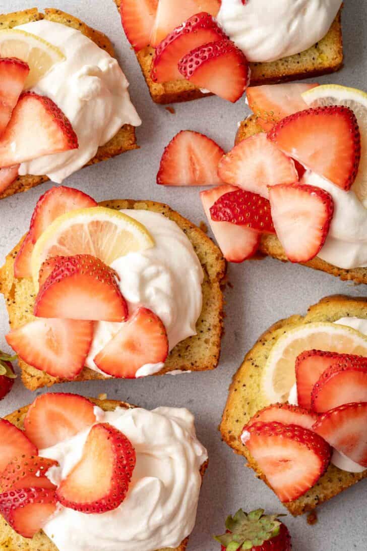 Slices of pound cake topped with Mascarpone Whipped Cream. Slices of strawberries are scattered over the cream.