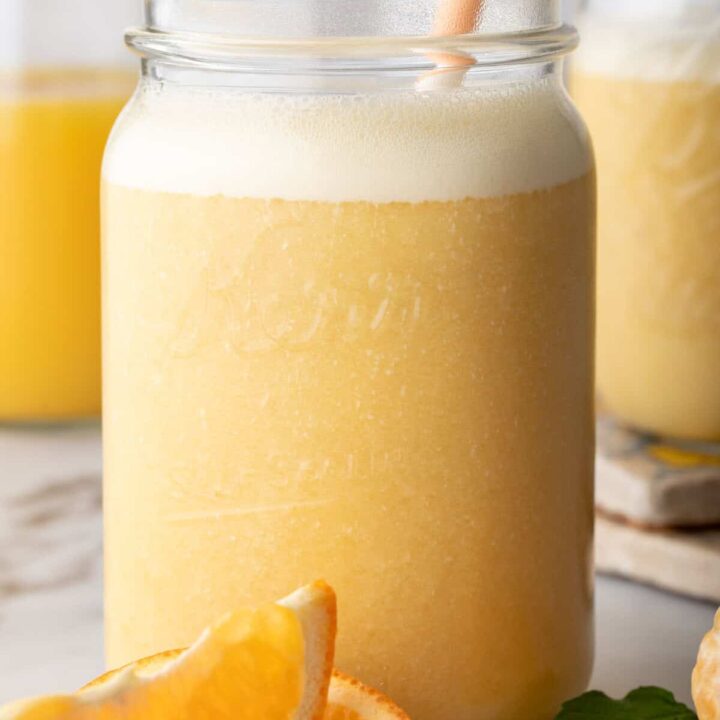 A clear mason jar filled with Orange Smoothie. A white and orange striped straw is in the jar.