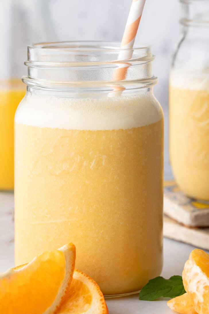 A clear mason jar filled with Orange Smoothie. A white and orange striped straw is in the jar.