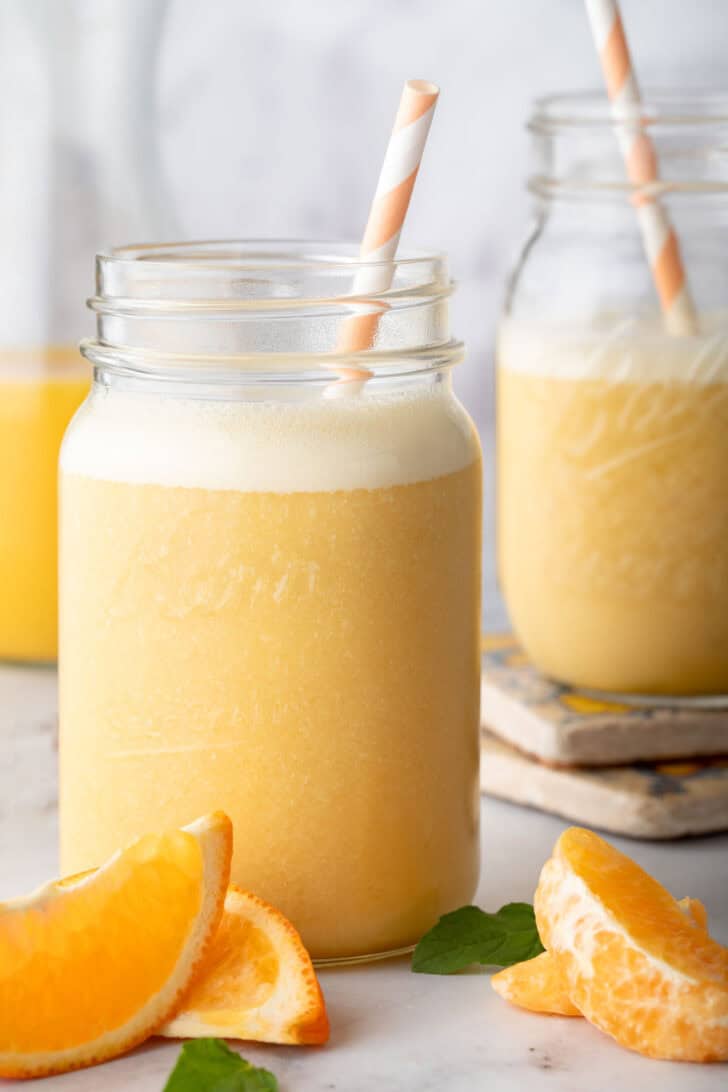 Two clear mason jars filled with Orange Smoothie. A white and orange striped straw are poked in both jars.