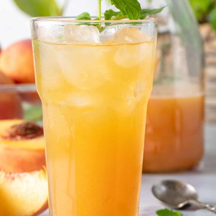 A clear drinking glass filled with Peach Green Tea.