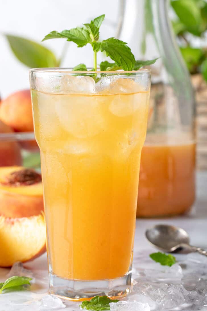 A clear drinking glass filled with Peach Green Tea.