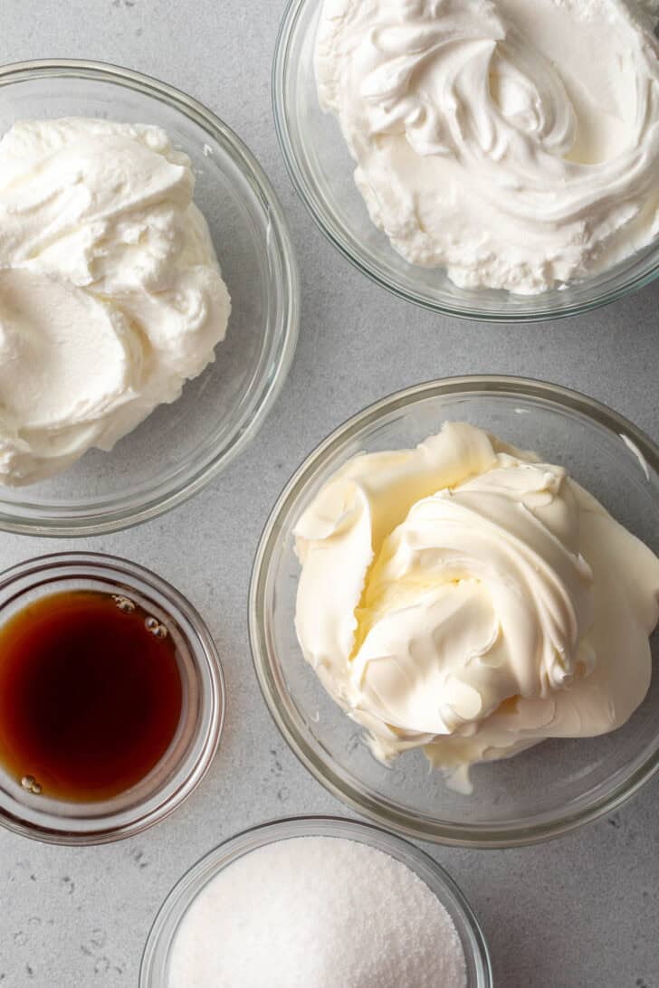 Five small glass bowls filled with cream, sour cream, yogurt, pure vanilla extract and granulated sugar.