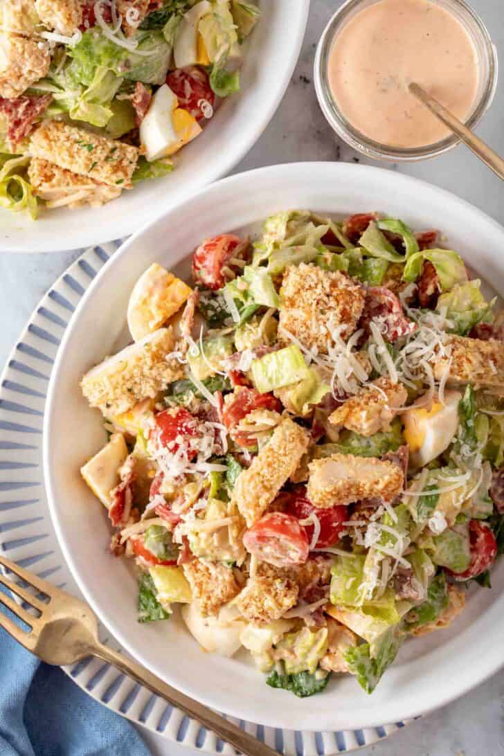 A white bowl filled with Crispy Chicken Salad. A small glass jar filled with Thousand Island Dressing sits next to the bowl.