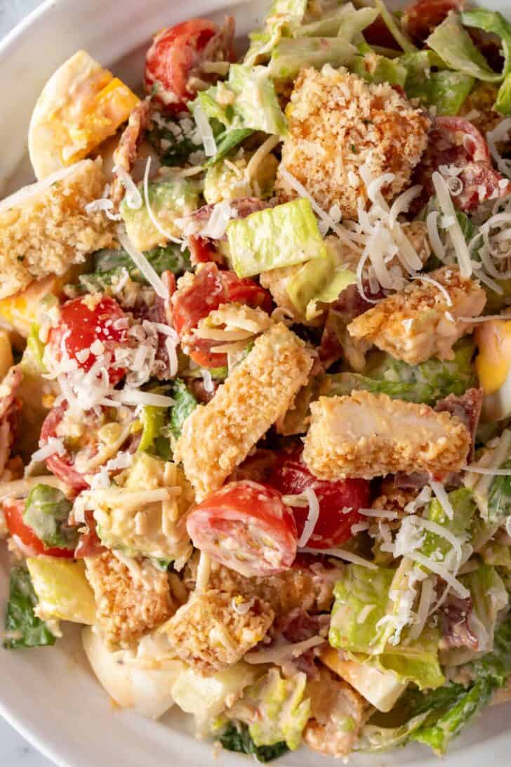 A white bowl filled with mixed greens, vegetables and oven baked chicken tenders.