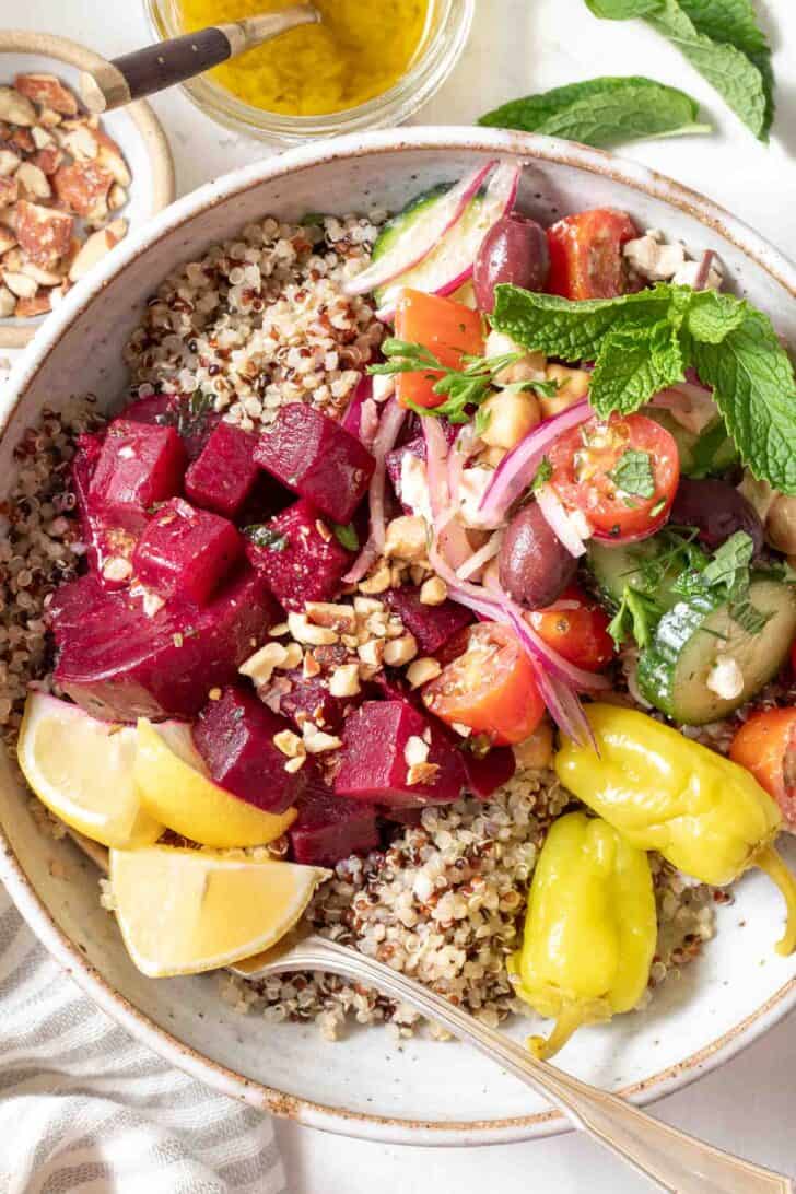 A white bowl filled with quinoa, marinated beets and Greek cucumber salad for a Mediterranean bowl.