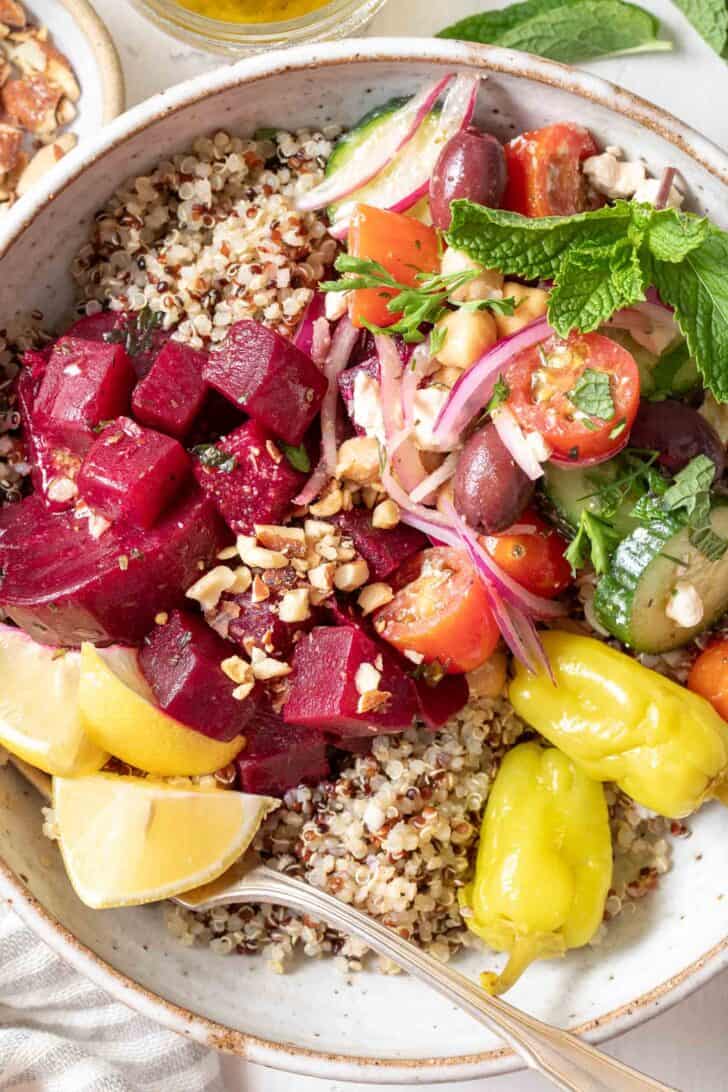 A white bowl filled with cooked quinoa, Greek cucumber salad and marinated beets for a Mediterranean Bowl.