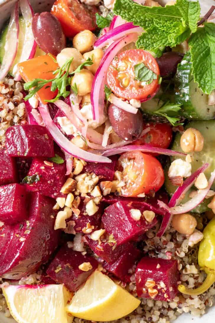 A close up of a Mediterranean bowl filled with marinated beets, cooked quinoa and Greek cucumber salad.