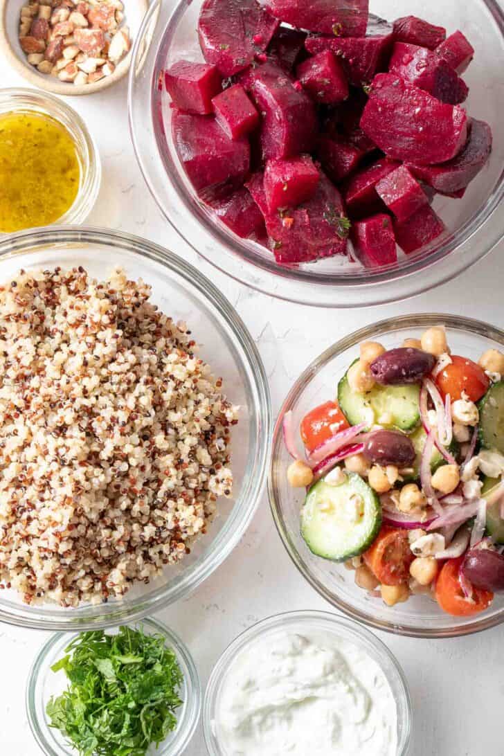 Glass mixing bowls filled with marinated beets, cooked quinoa, Greek salad and tzatziki sauce.