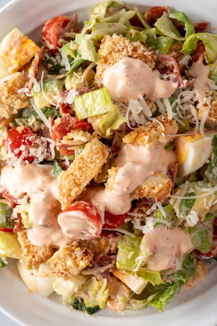 A white bowl filled with salad tossed with crispy chicken and cherry tomatoes.