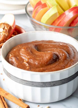 A white bowl filled with Caramel Apple Dip. A clear glass bowl filled with apple slices sits next to the bowl.