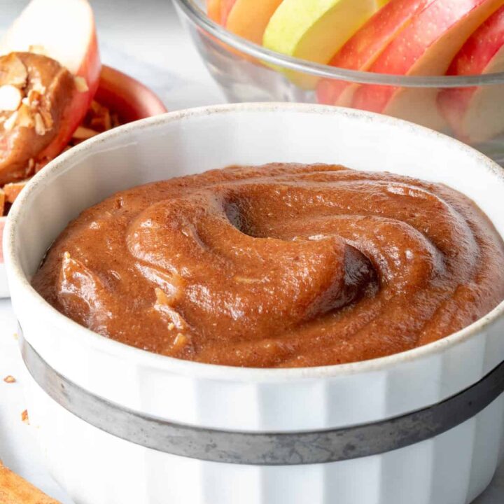 A white bowl filled with Caramel Apple Dip. A clear glass bowl filled with apple slices sits next to the bowl.